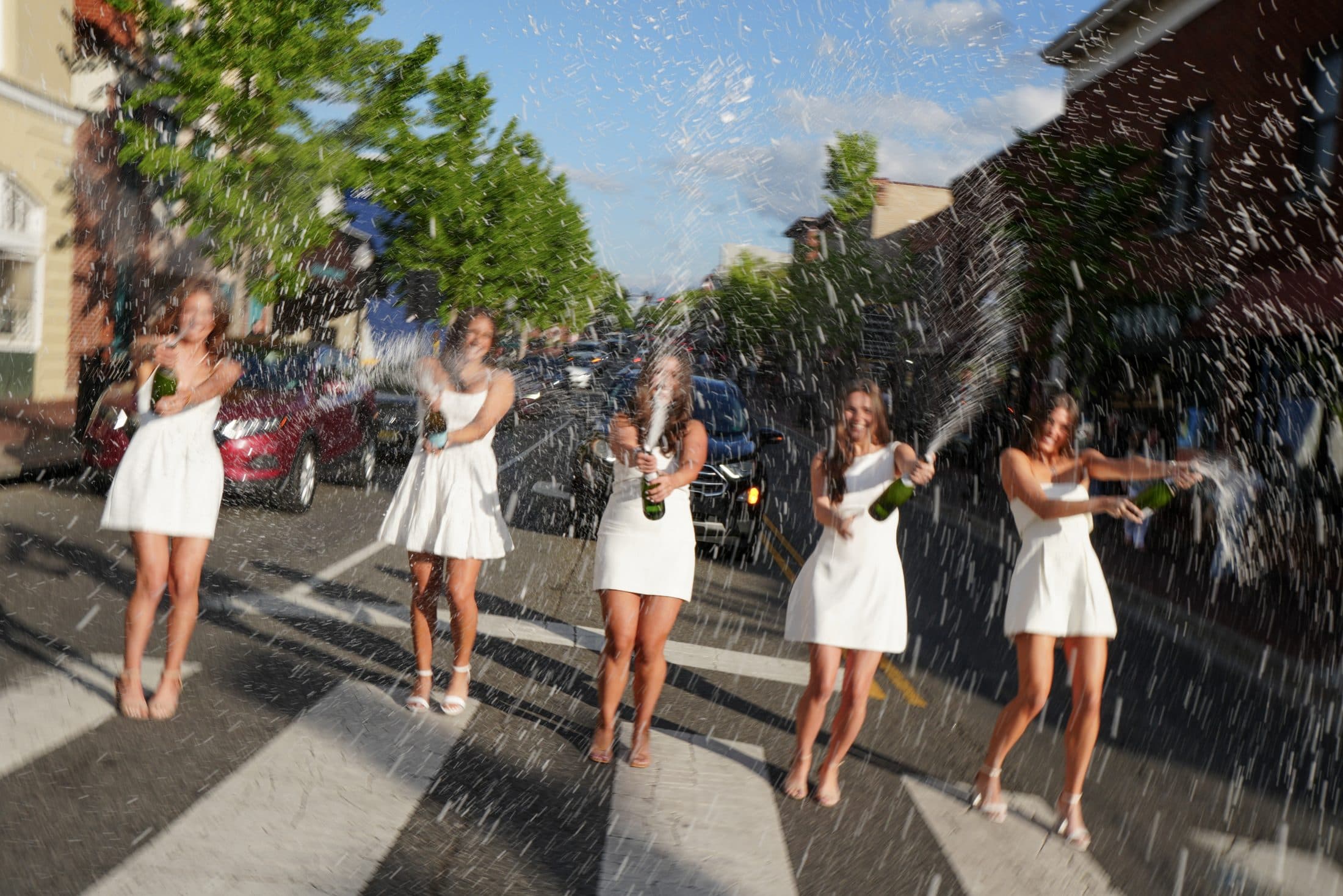 Five friends spraying champagne together in the middle of the street