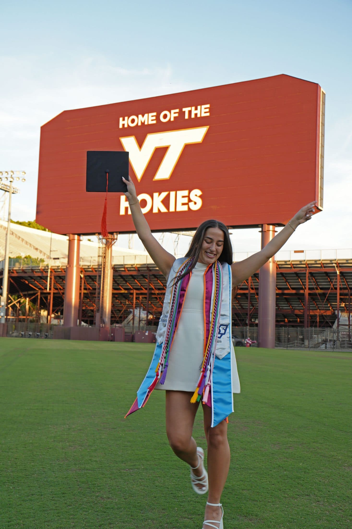 A graduate leaping mid-celebration across the stadium field