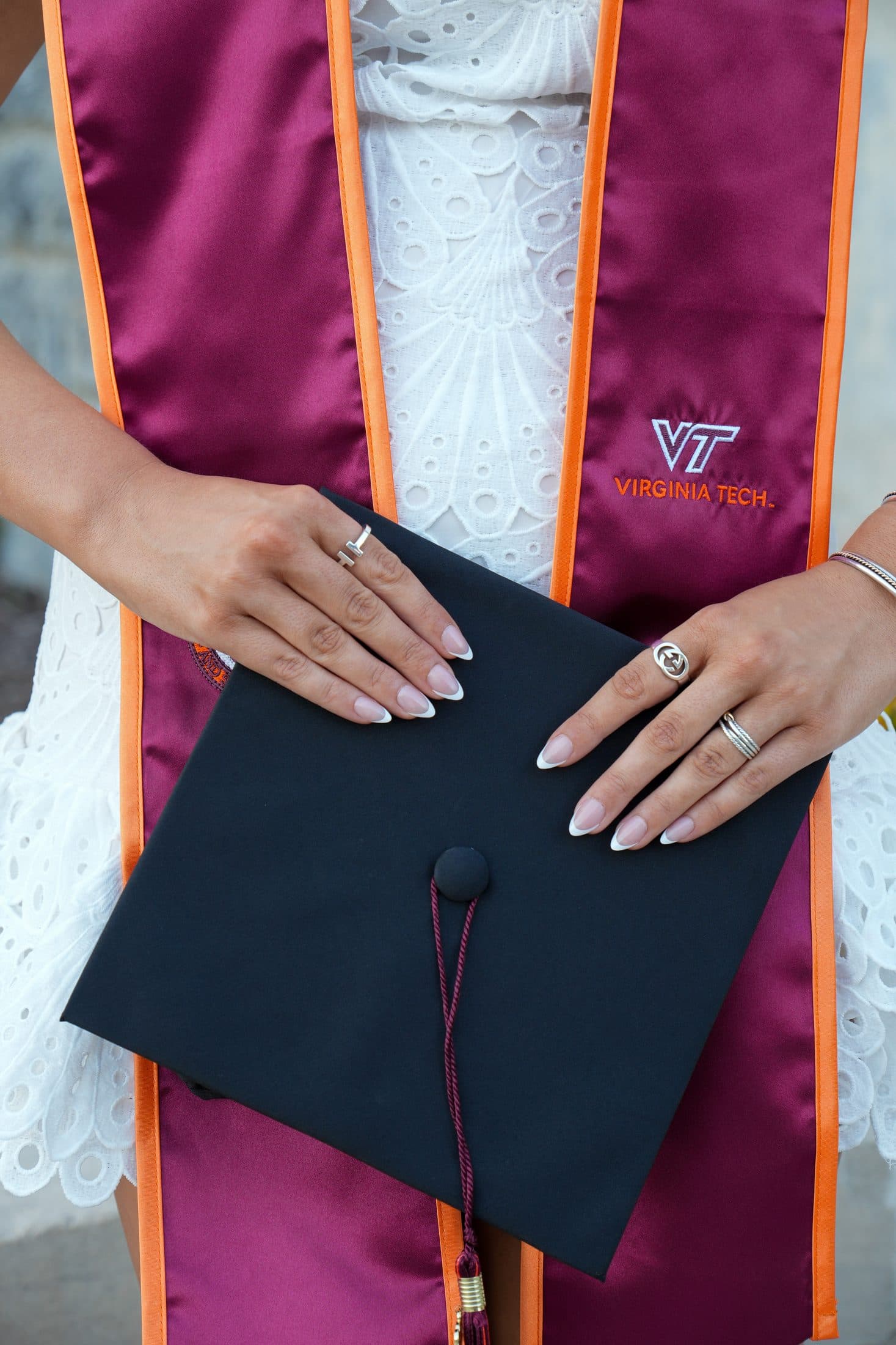 A tender close-up of hands resting on a graduation cap, rings catching the light